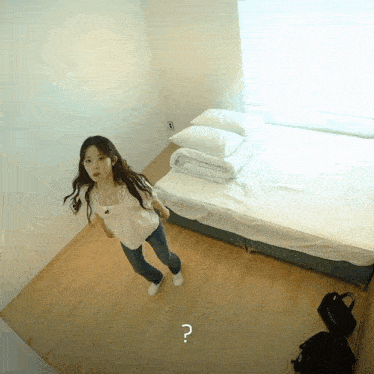 a woman is standing in front of a bed with a question mark on the floor