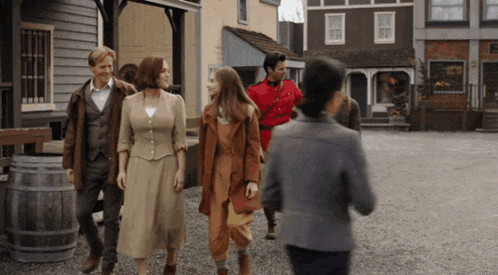 a group of people are walking down a street with a man in a red uniform