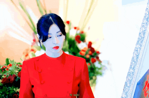a woman in a red dress is standing in front of flowers and a mirror .