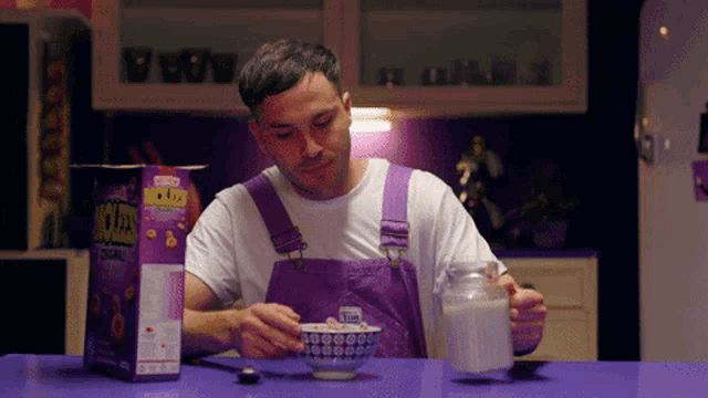 a man in purple overalls is eating a bowl of cereal from a box that says lucky charms