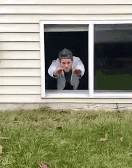 a man is sticking his head out of a window in a yard .