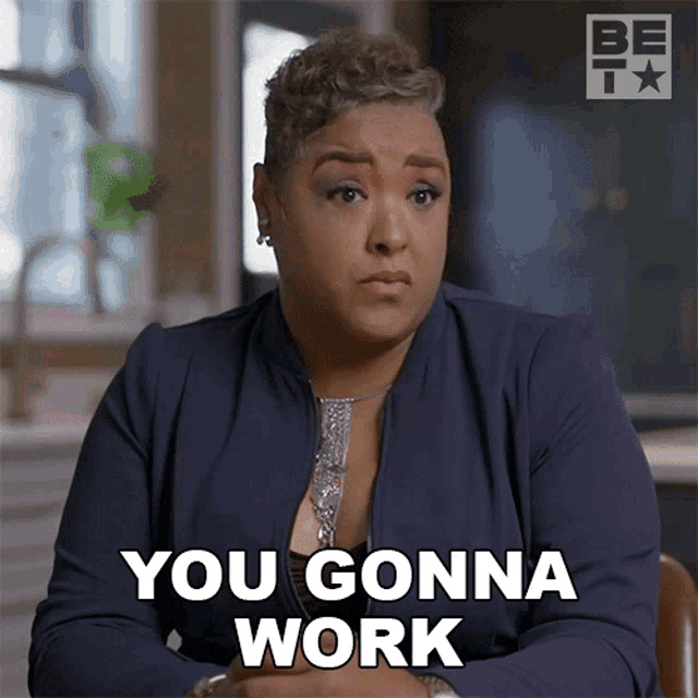 a woman in a blue jacket is sitting at a table and says " you gonna work "