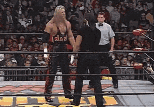 two wrestlers are standing in a wrestling ring with a referee in the background .