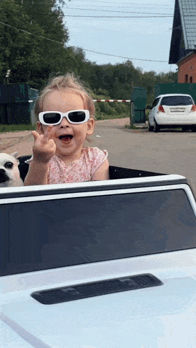 a little girl wearing sunglasses is giving the middle finger while sitting in a car