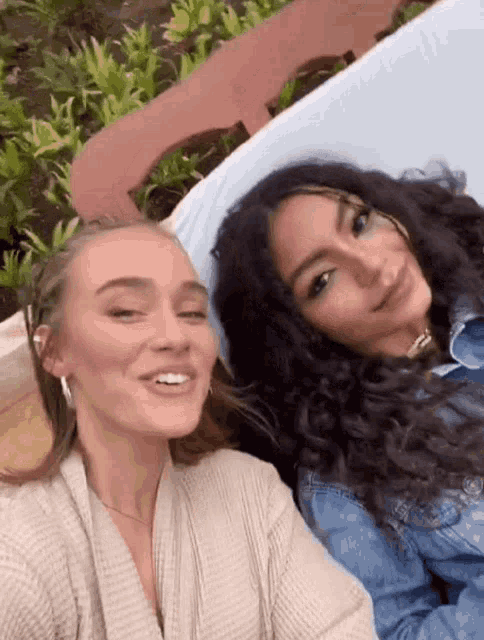 two women are laying next to each other on a couch and smiling for the camera .