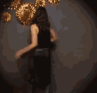 a woman in a black top and blue jeans is dancing in front of gold pom poms