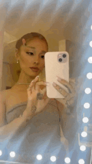 ariana grande is taking a selfie with her phone in a mirror .