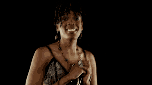 a woman singing into a microphone with her hands folded in front of her face