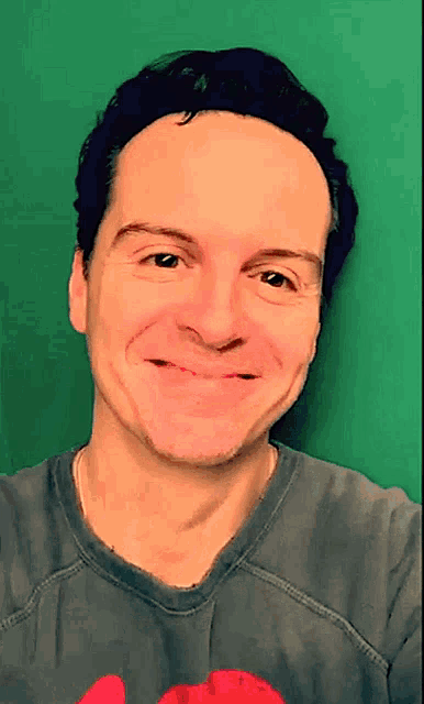 a man wearing a grey shirt with a red heart on it is smiling