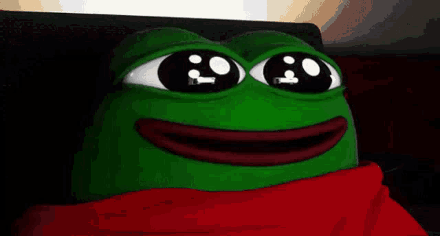 a green frog with big eyes is wearing a red scarf around its neck .