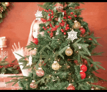 a woman is standing in front of a christmas tree