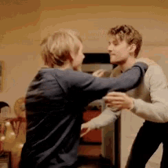 two men are standing next to each other and hugging each other in a living room .