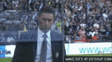 a man in a suit and tie is standing on a soccer field in front of a crowd