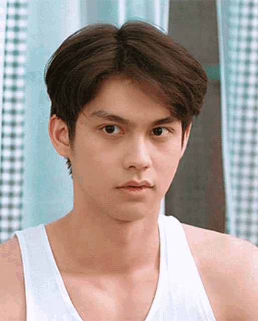 a young man in a white tank top looks at the camera .