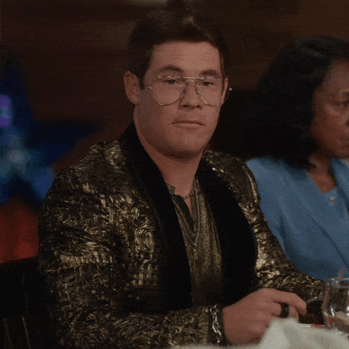 a man wearing glasses and a gold jacket sits at a table with a woman