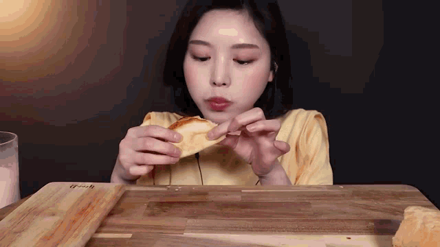 a woman in a yellow shirt is eating a piece of bread on a wooden cutting board .