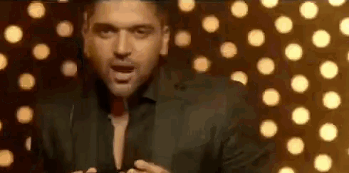 a man in a suit is standing in front of a wall of lights and singing into a microphone .