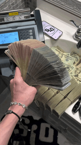 a person holding a bunch of money in front of a counter with a phone on it that says ' 5 ' on it