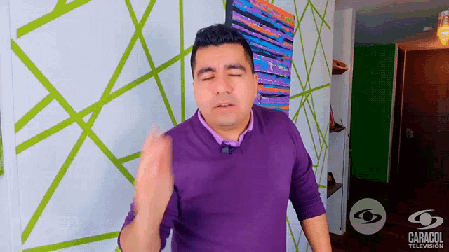 a man wearing a purple sweater is standing in front of a caracol television sign