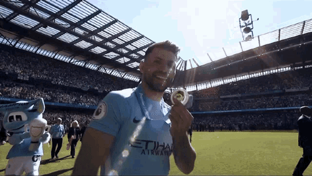 a man in a blue etihad airways jersey holds a medal