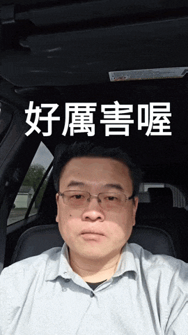 a man wearing glasses is sitting in a car with chinese characters behind him