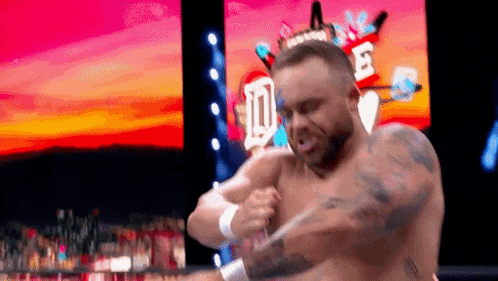 a shirtless wrestler is standing in front of a crowd on a stage .