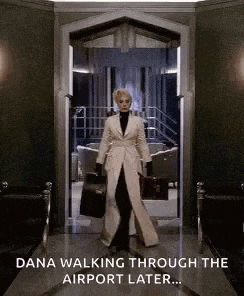 a woman in a white coat and black pants is walking through a doorway holding a suitcase .
