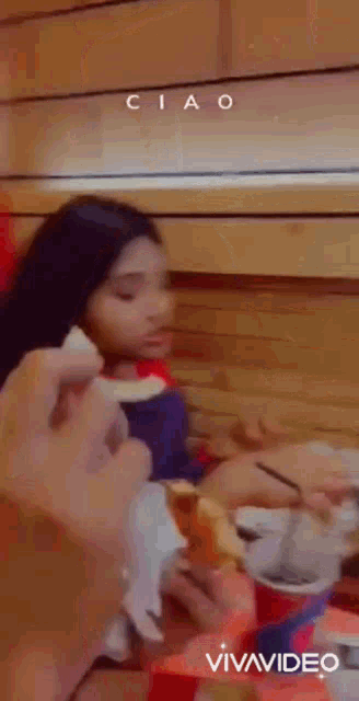 a girl is sitting at a table eating a sandwich and a person is holding a piece of bread .