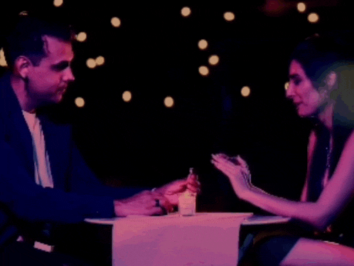 a man and woman are sitting at a table with a shot glass