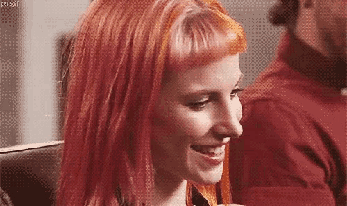 a woman with red hair is smiling and looking at the camera while sitting in a chair .