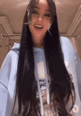 a woman with long black hair is wearing a light blue hoodie and smiling .