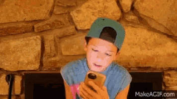 a young boy wearing a baseball cap is looking at his phone