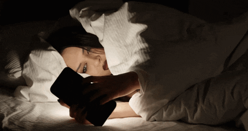 a woman laying in bed using a cell phone