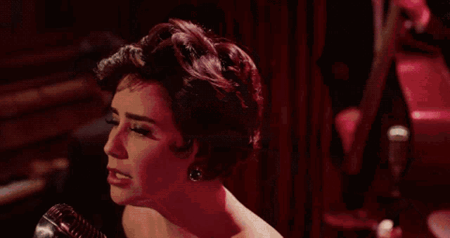 a woman is singing into a microphone with a red light behind her