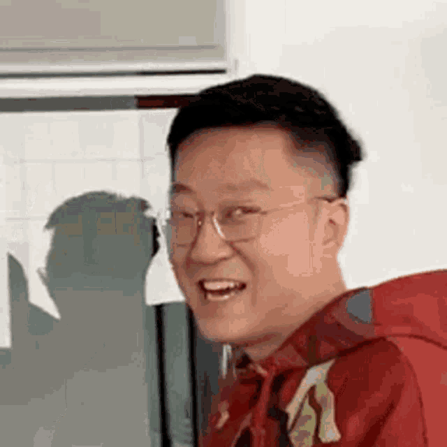 a man wearing glasses and a red hoodie is smiling and making a funny face .