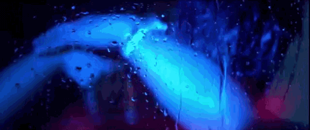a person is standing in front of a window with rain drops on it and a blue light behind them .