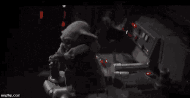a baby yoda is sitting on a control panel in a dark room in a star wars movie .