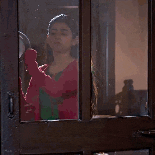 a woman in a pink and green dress is looking out of a window