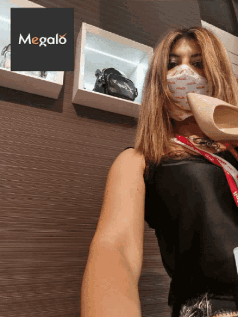 a woman wearing a face mask holds a shoe in front of a sign that says megalo