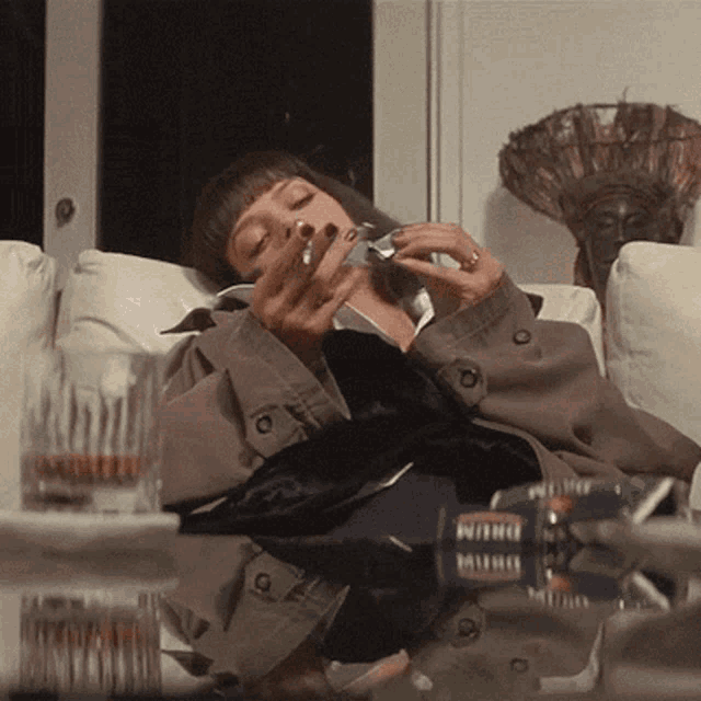 a woman is laying on a couch smoking a cigarette and drinking from a bottle of milwaukee