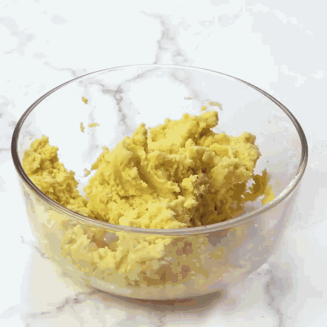 a glass bowl filled with mashed potatoes on a marble surface