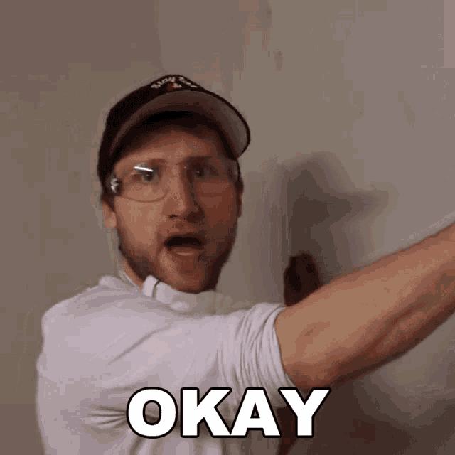 a man wearing glasses and a hat with the word okay on his shirt