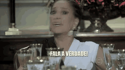 a woman is sitting at a table with glasses and a sign that says fala a verdade