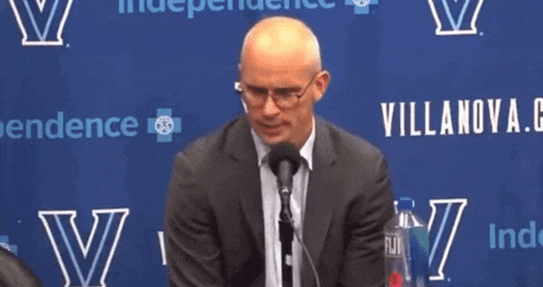 a man in a suit is speaking into a microphone in front of a villanova banner