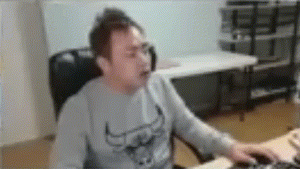 a man is sitting at a desk using a computer mouse and yawning .