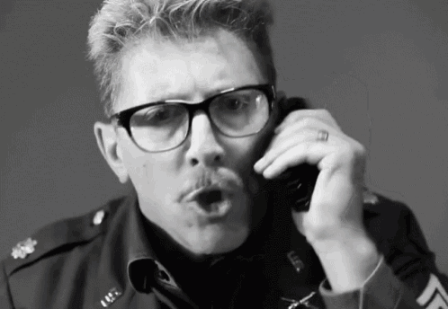 a man in a military uniform is talking on a phone with the letter l on his sleeve