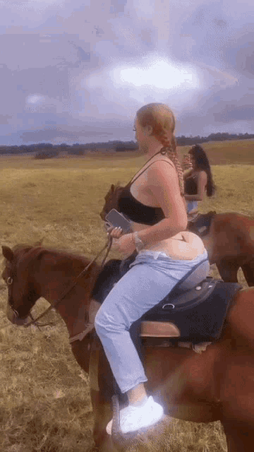 a woman riding a brown horse in a field holding a cell phone