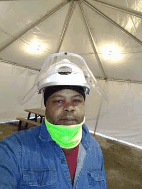a man wearing a hard hat and a neon green scarf takes a selfie in a tent .