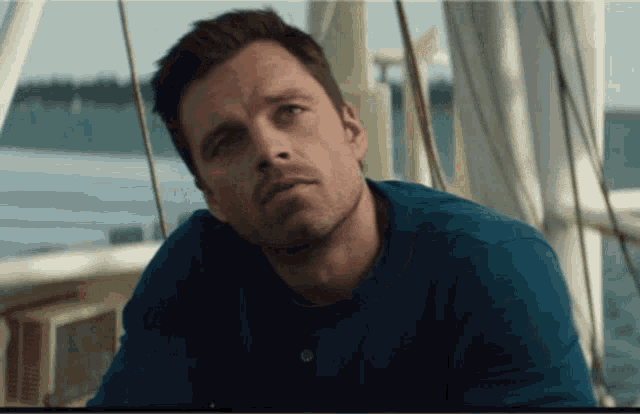 a man in a blue shirt is sitting on a boat near the water