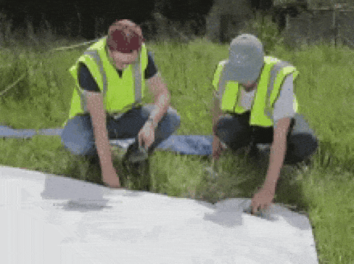 two men wearing safety vests are working on a piece of paper in a field